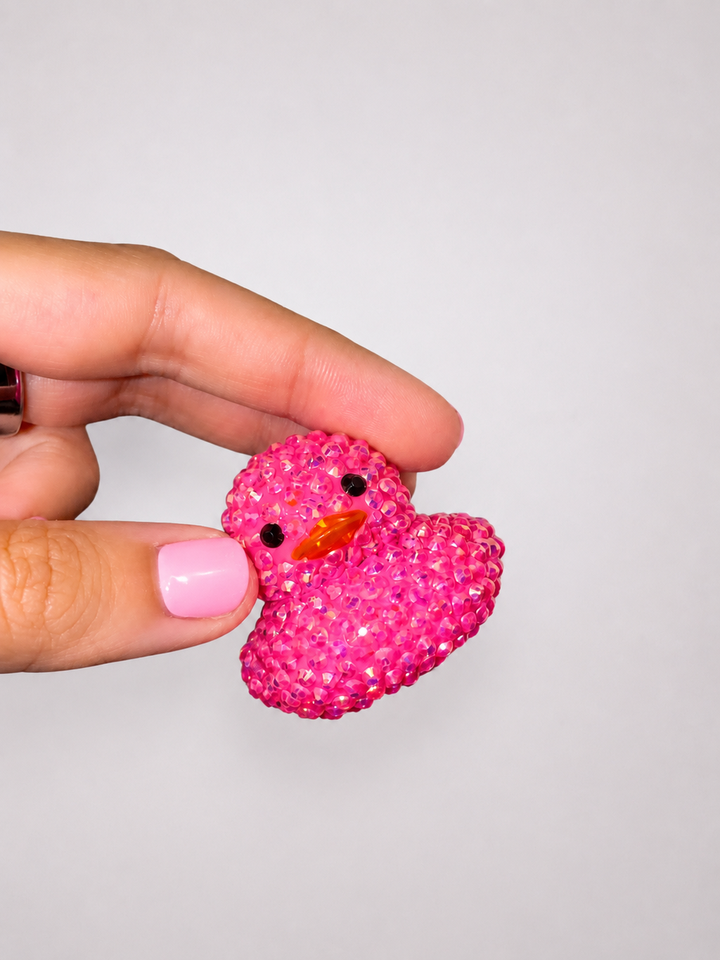 Pink rhinestoned rubber duck held by a hand against a light gray background