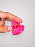 Pink rhinestoned rubber duck held by a hand against a light gray background