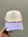 Colorful cap with a rainbow brim held by a hand against a plain background
